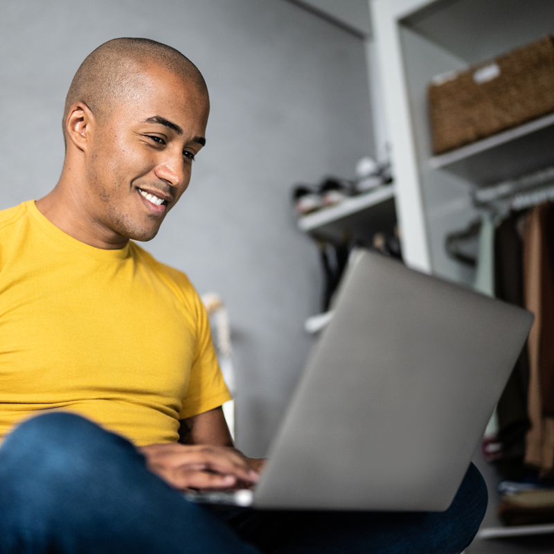 smiling young man in yellow shirt reading something on his laptop