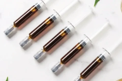 Unbranded cannabis oil cartridges arranged beside green leaves
